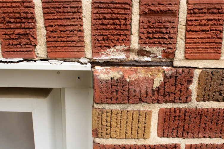 A close-up of brickwork near a window, showing cracks.