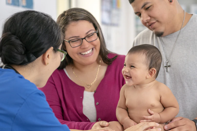 Health care practitioner conducting a checkup on a baby being held by the parents.