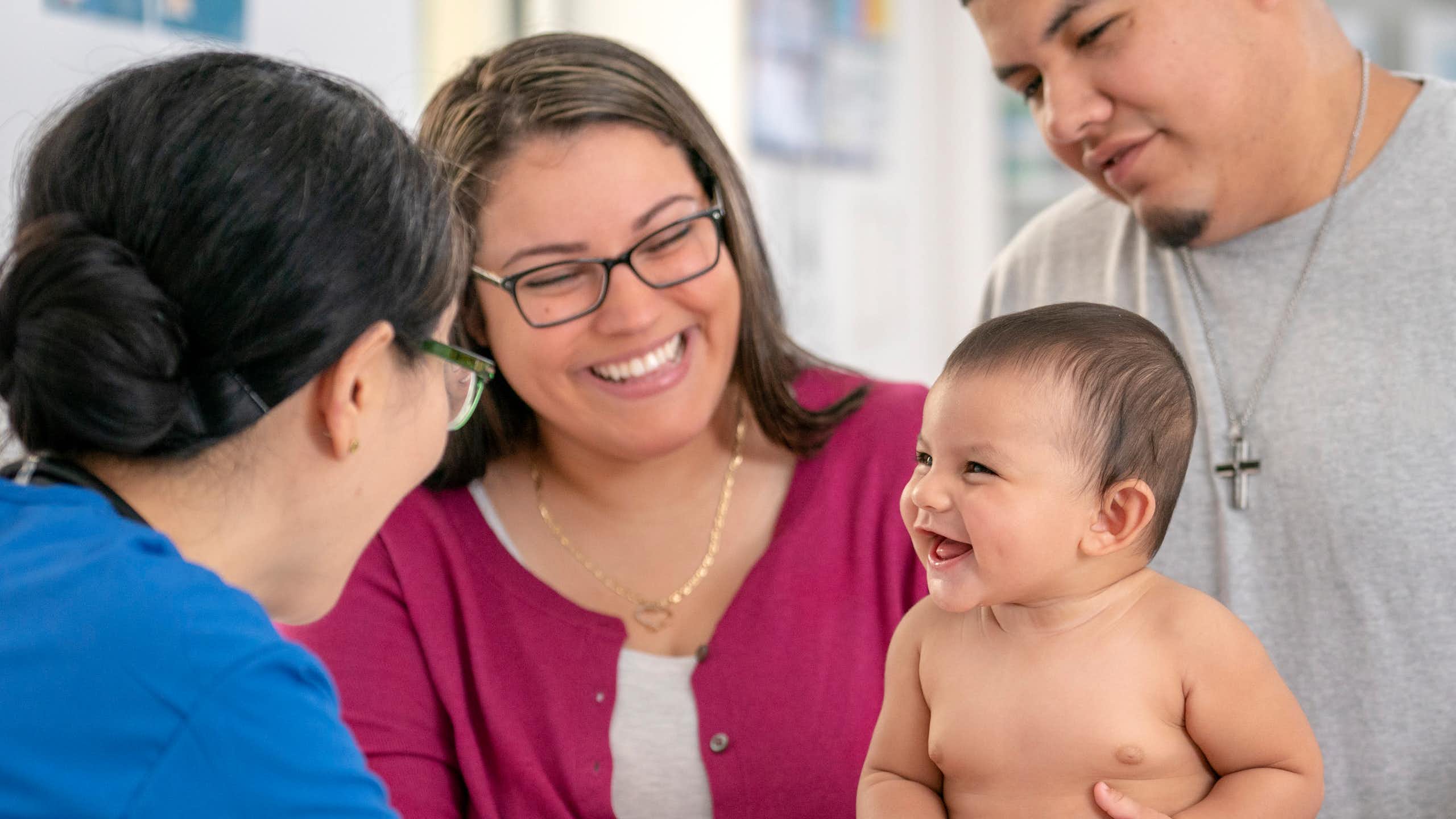 Health care practitioner conducting a checkup on a baby being held by the parents.