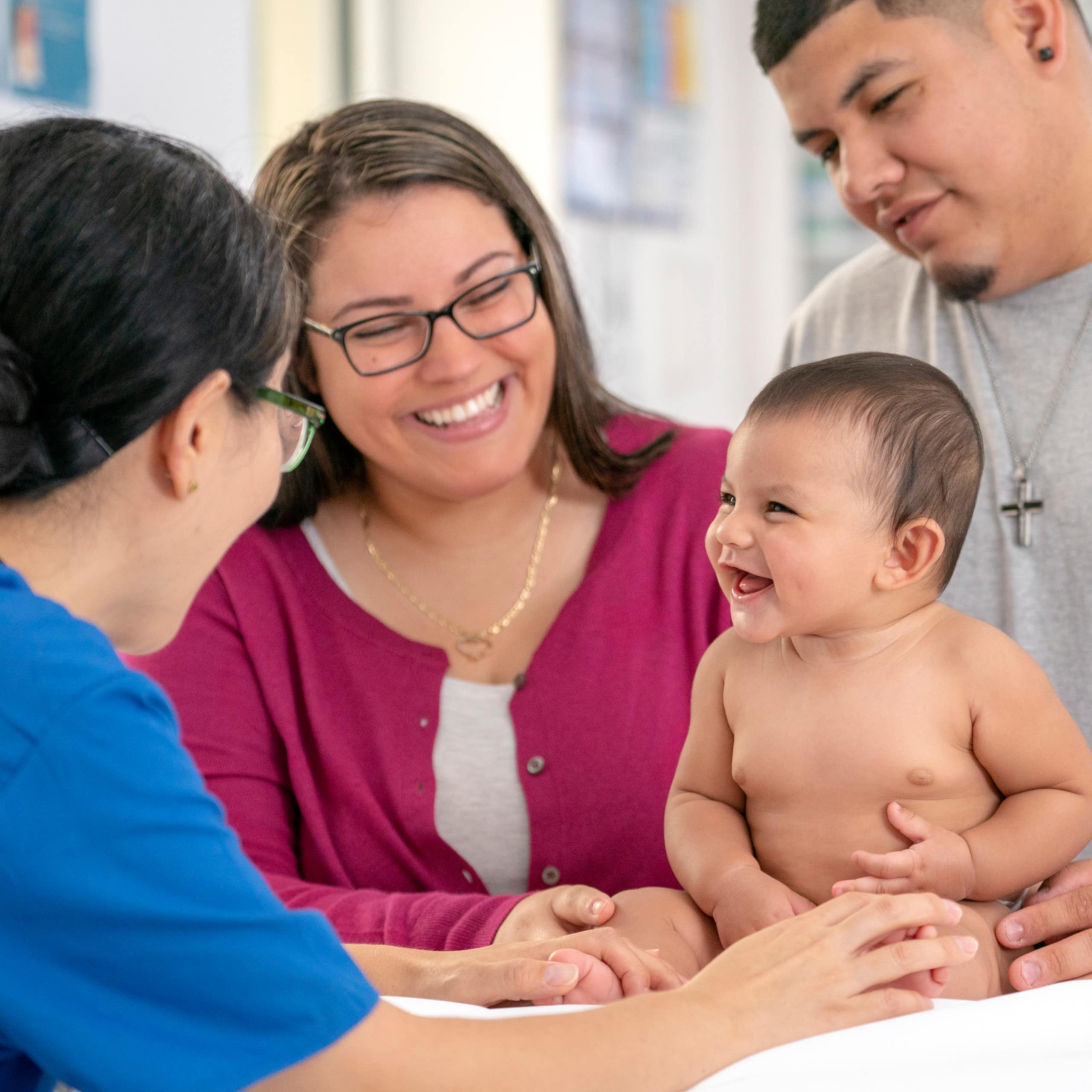 Health care practitioner conducting a checkup on a baby being held by the parents.