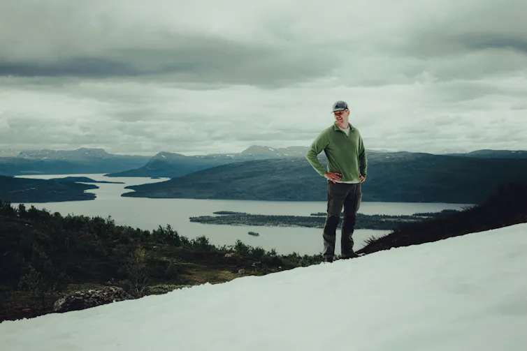A man stands with his hands on hips while hiking in snow.