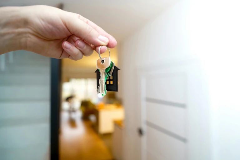 A woman's hand holding a set of house keys on the threshold of a home