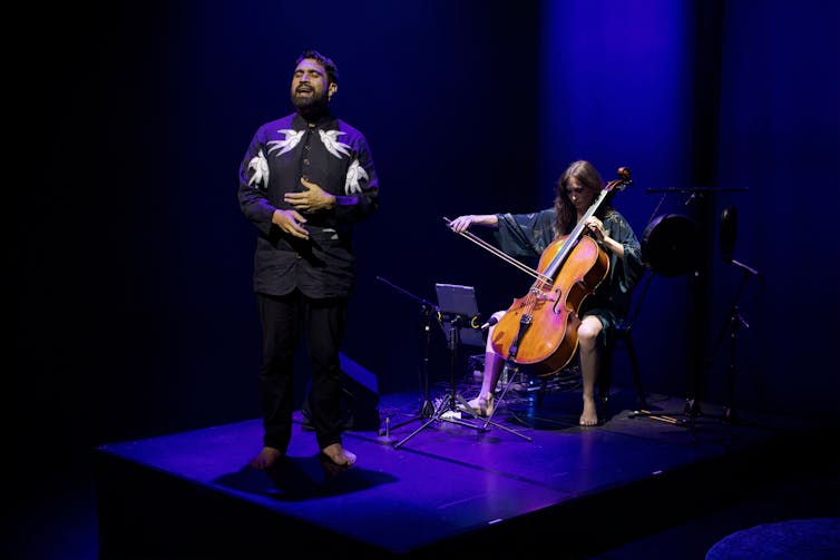 A man sings, a woman plays the cello.