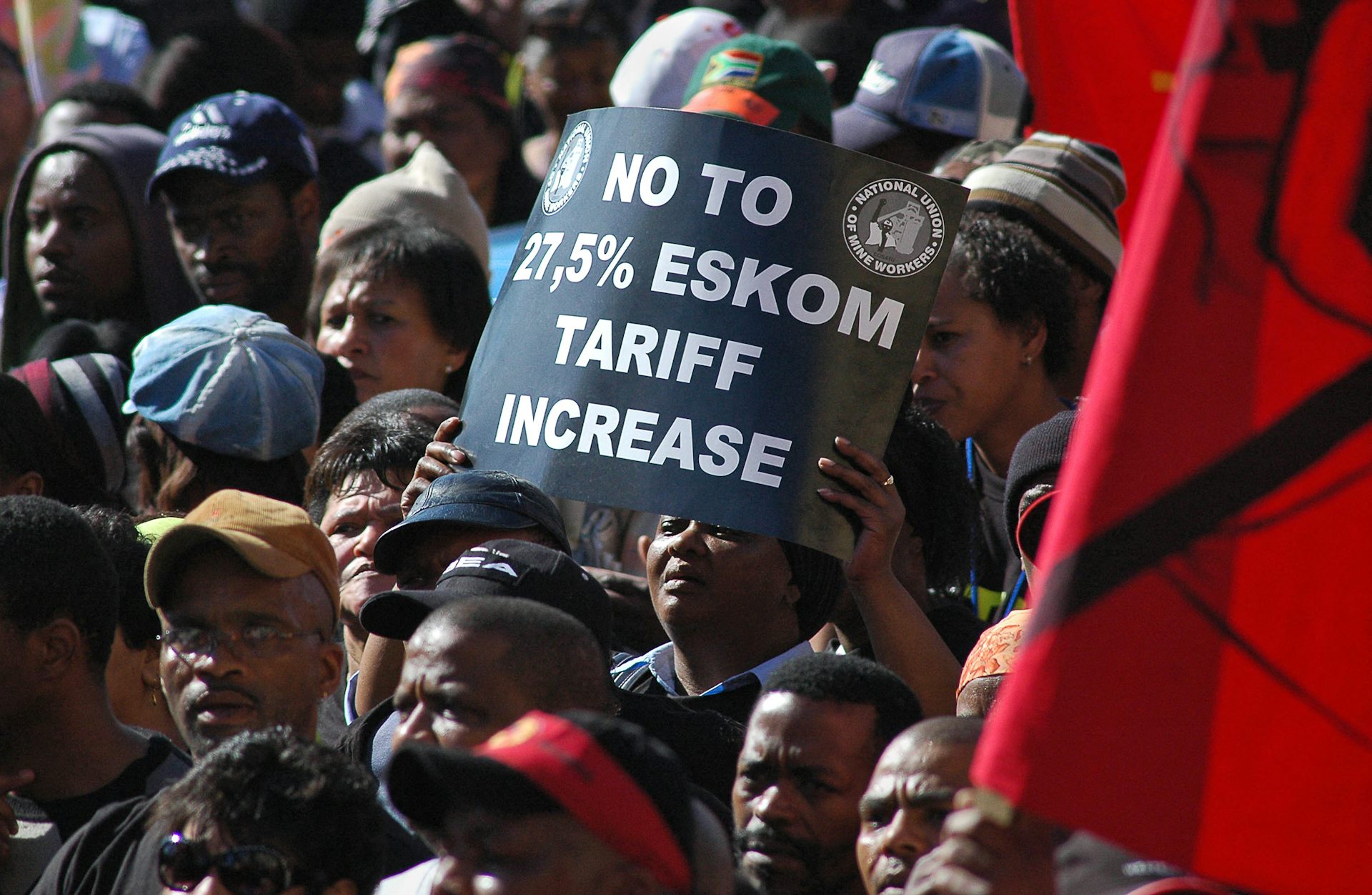 Closely grouped people, one holding up a sign that says 'No to 27.5% Eskom tariff increase'