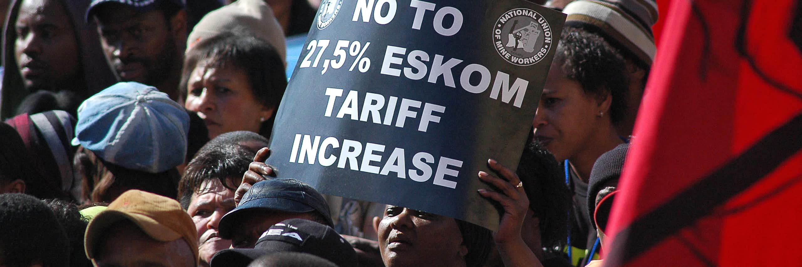 Closely grouped people, one holding up a sign that says 'No to 27.5% Eskom tariff increase'