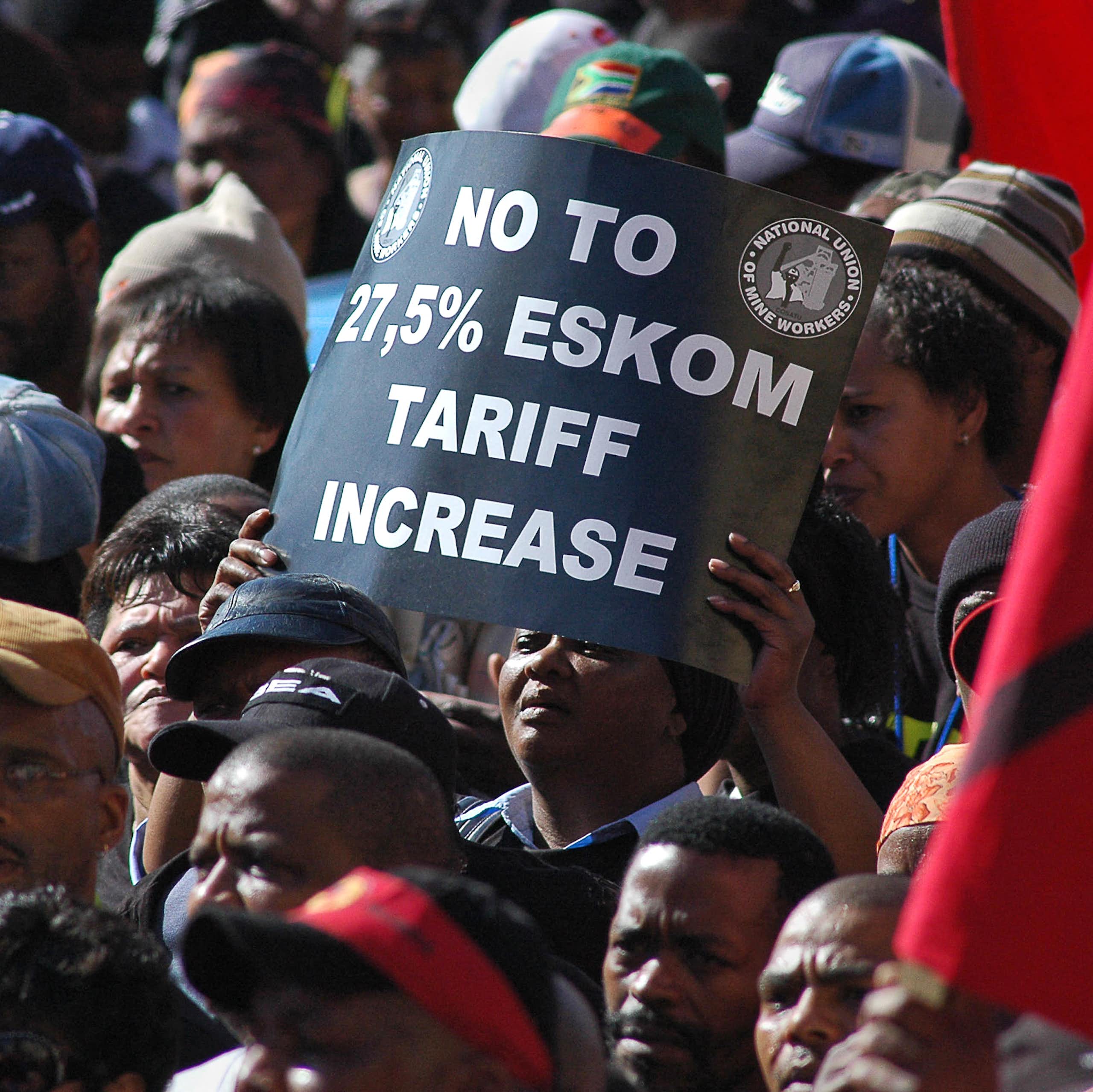 Closely grouped people, one holding up a sign that says 'No to 27.5% Eskom tariff increase'