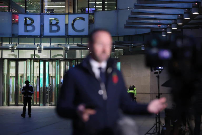 A reporter, out of focus, outside of BBC broadcasting house in the evening