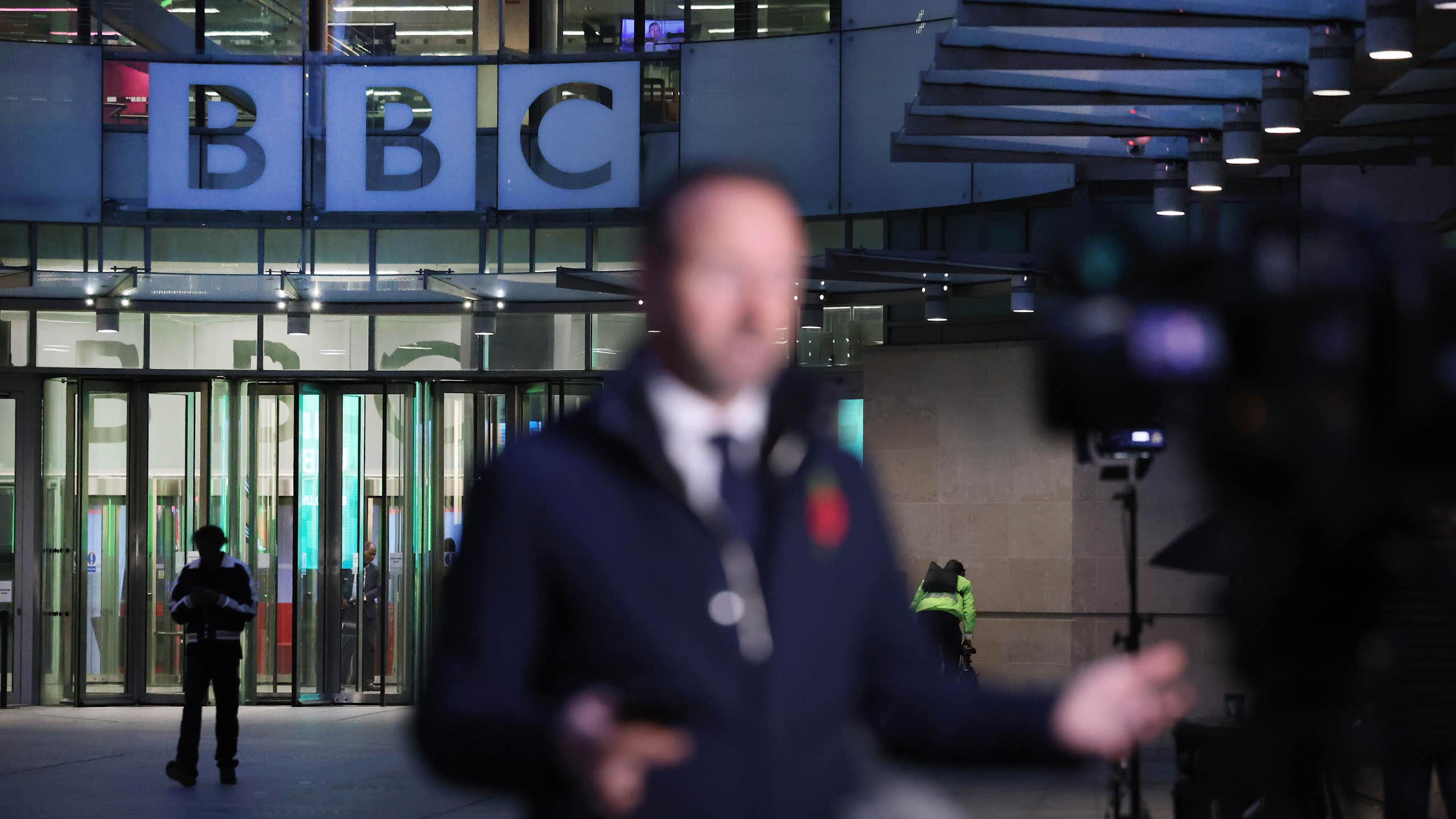 A reporter, out of focus, outside of BBC broadcasting house in the evening