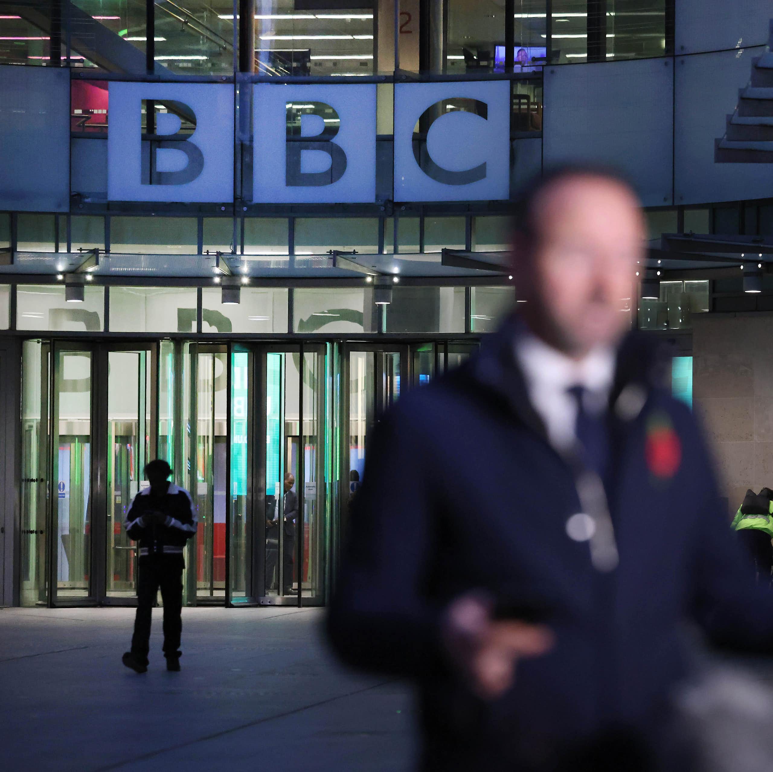 A reporter, out of focus, outside of BBC broadcasting house in the evening