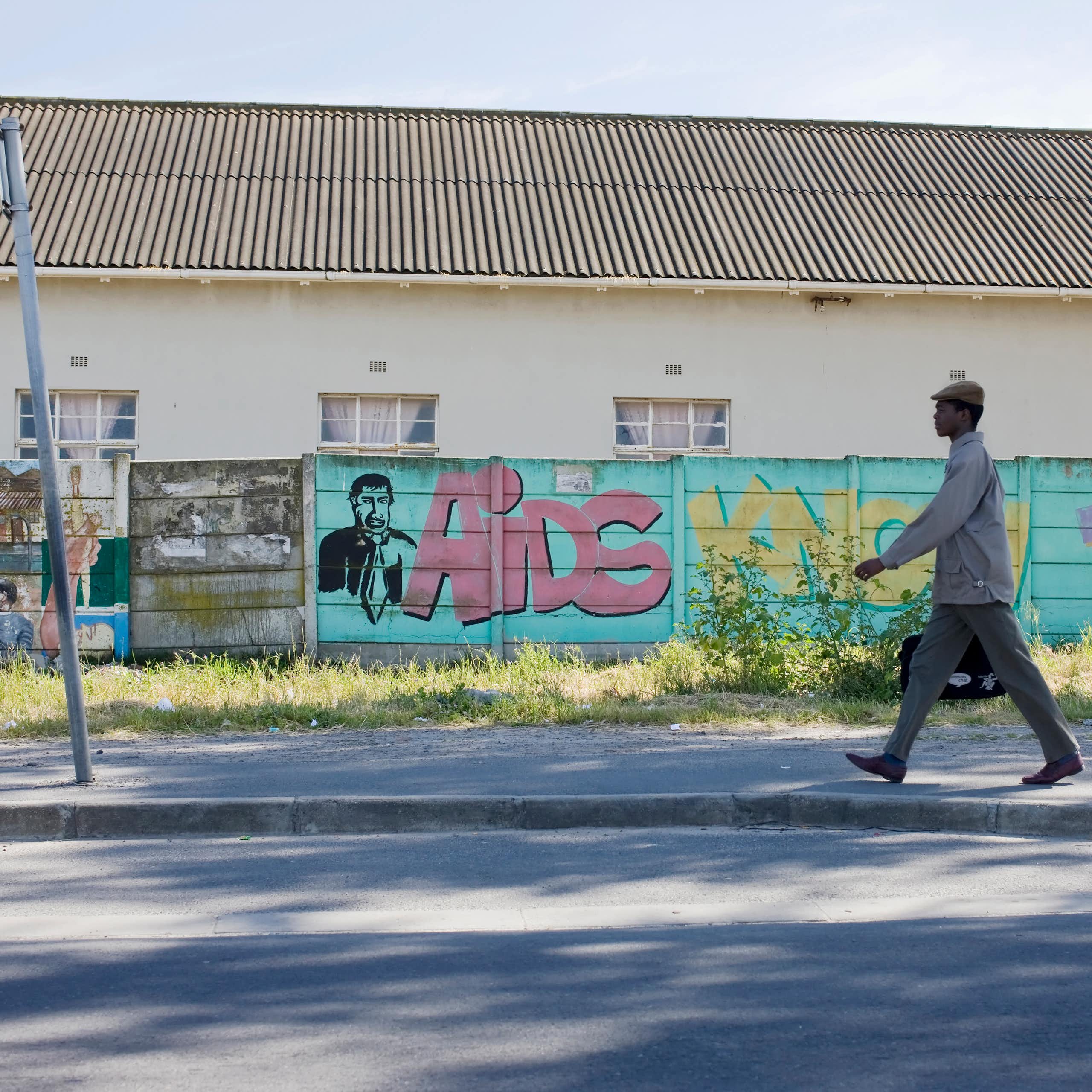 A wide shot of a wall with graffitti and a young African man walking resolutely in work clothes.