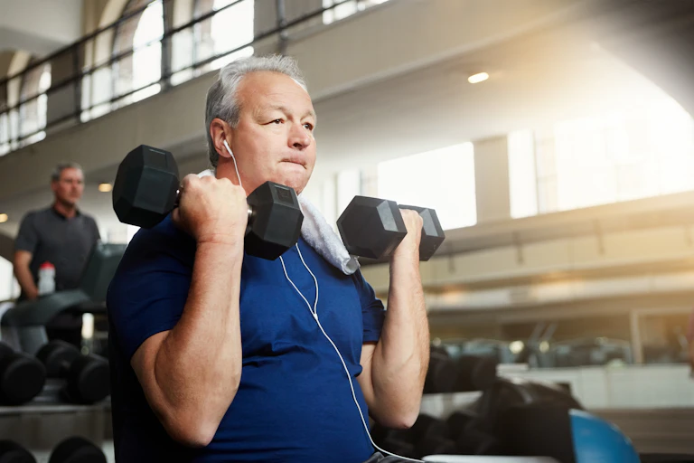 An older, overweight man performs dumbbell curls in the gym.