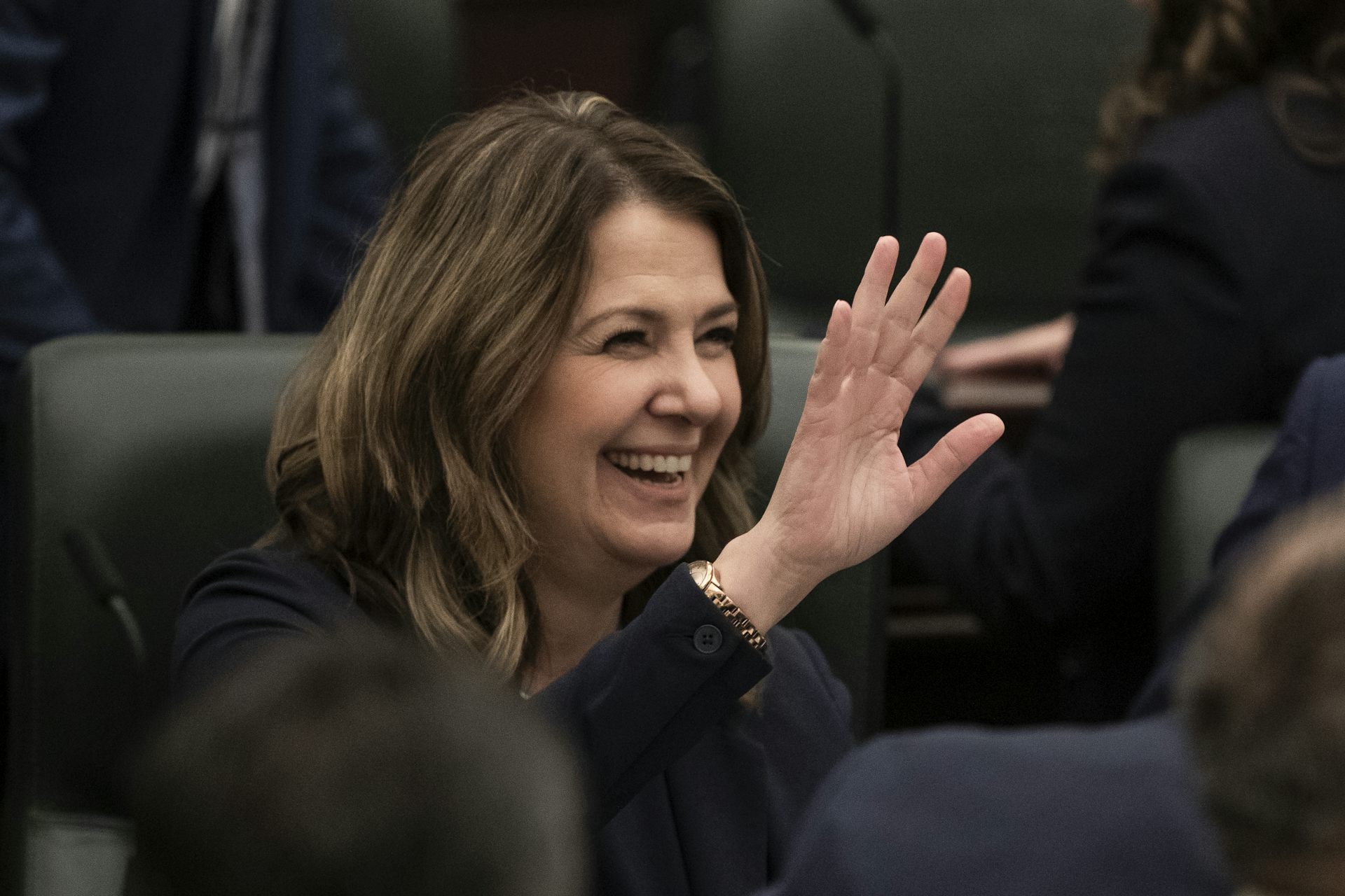 A dark-haired woman smiles and waves.