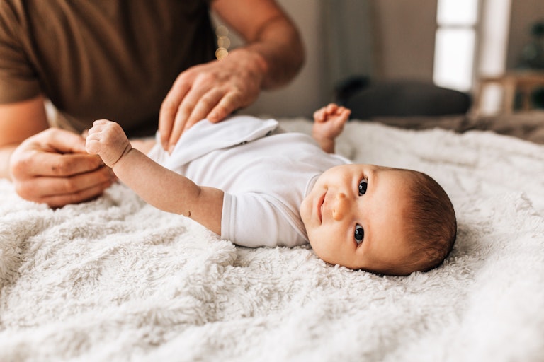 A man changes a baby's nappy on a bed.