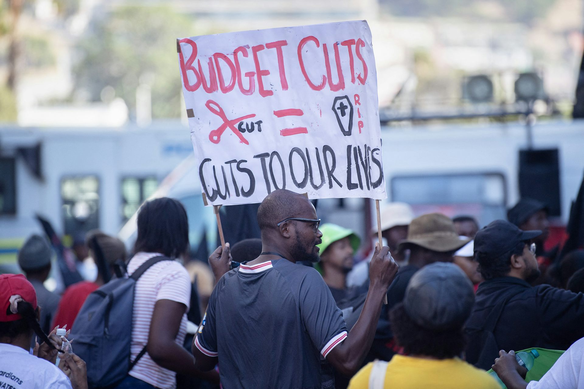 Group of people, one holding up a banner saying 'Budget cuts = cuts to our lives"