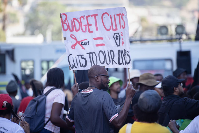 Group of people, one holding up a banner saying 'Budget cuts = cuts to our lives"