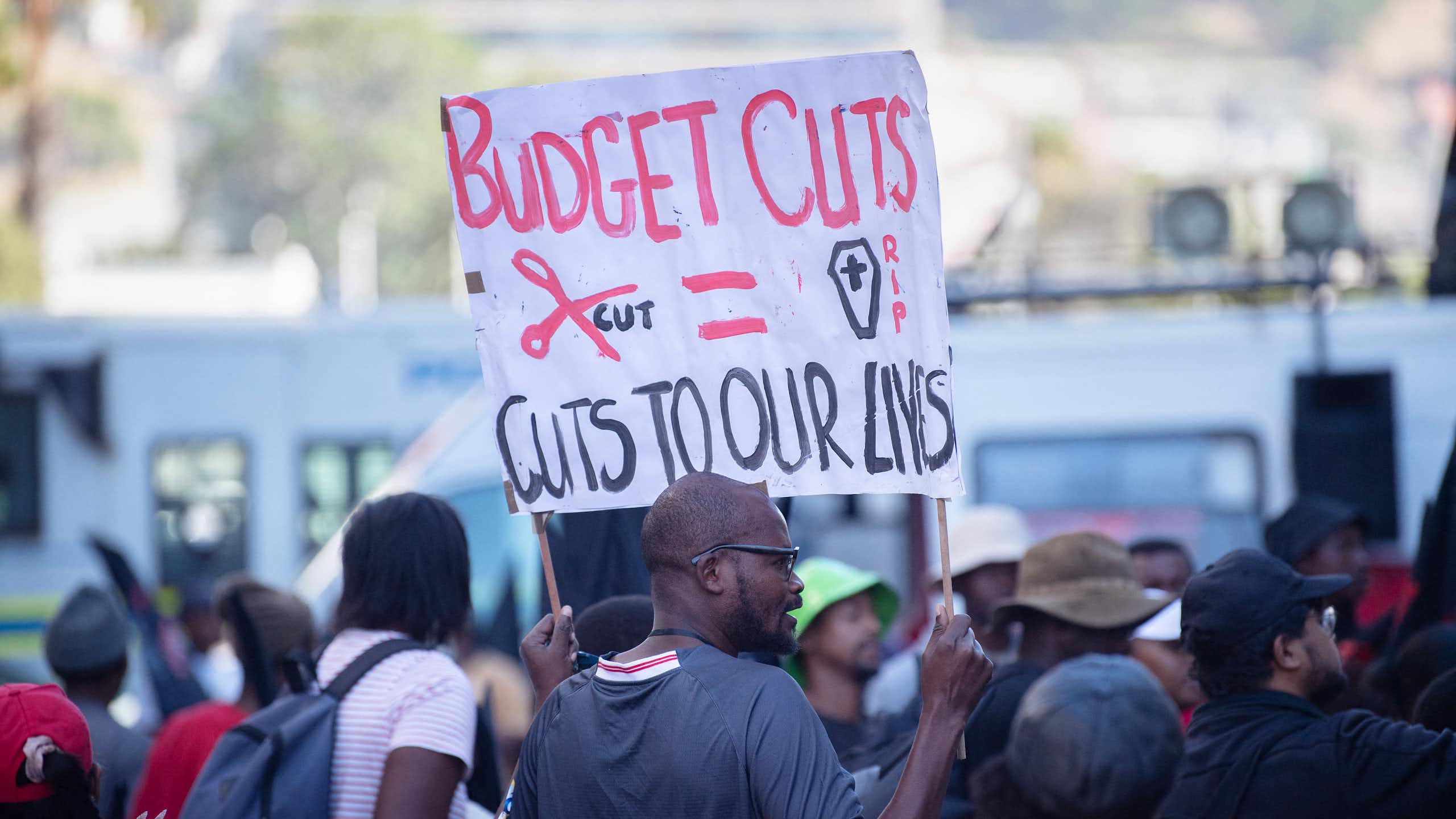 Group of people, one holding up a banner saying 'Budget cuts = cuts to our lives"