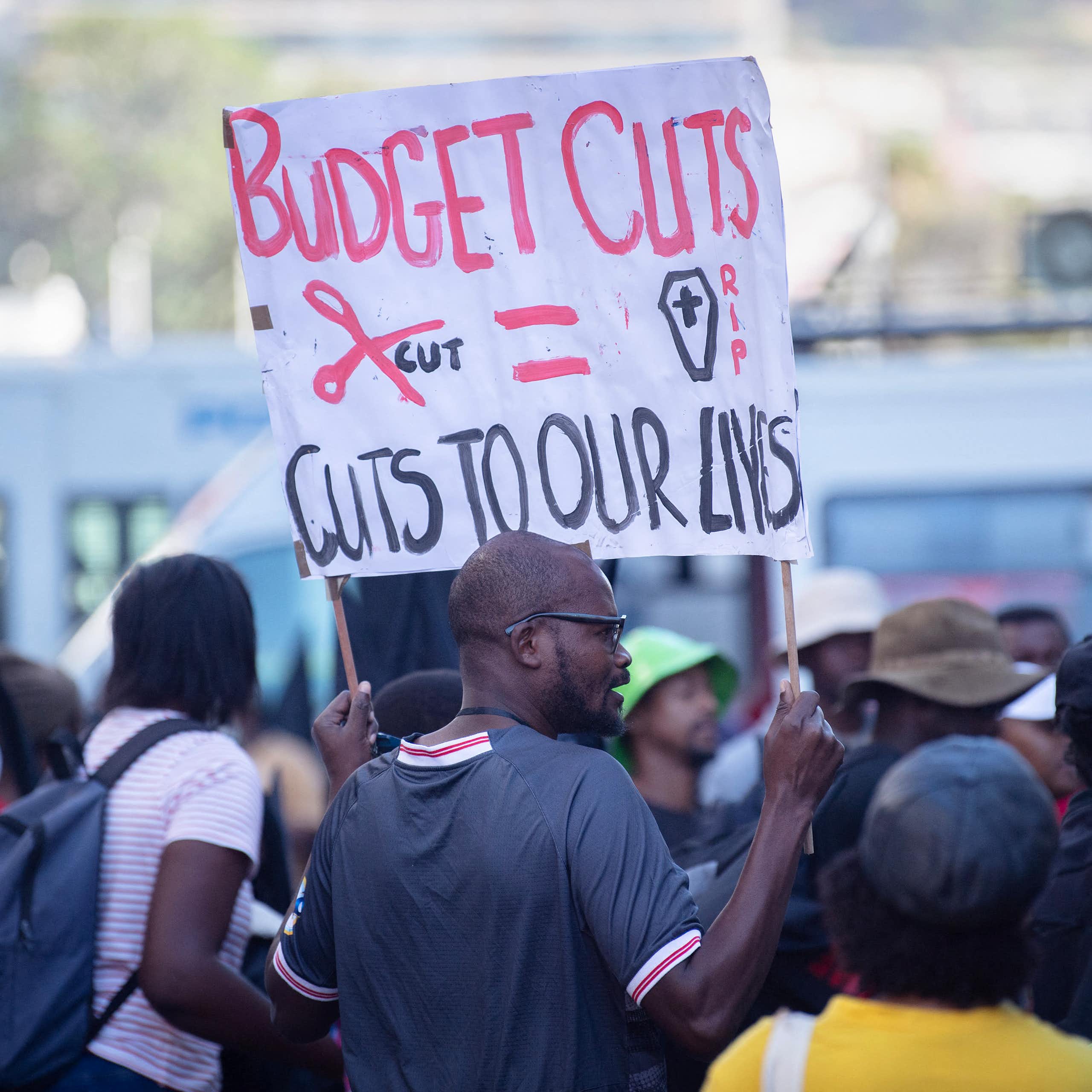 Group of people, one holding up a banner saying 'Budget cuts = cuts to our lives"