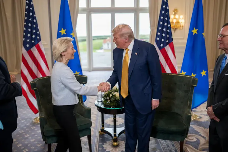 donald trump and ursula von der leyen shake hands in front of their respective flags.