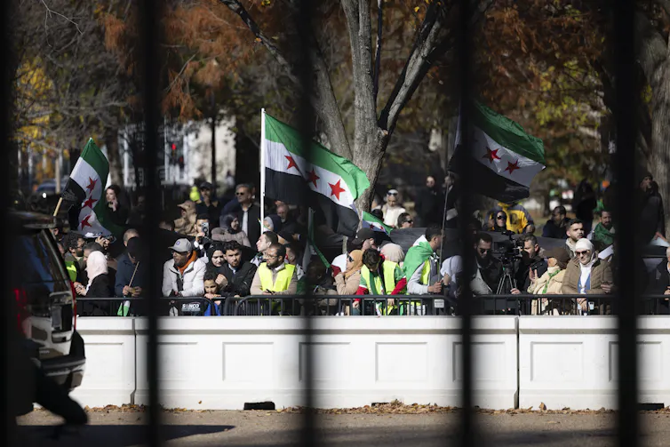A crowd of people waving Syrian national flags gathered outside the White House gates.