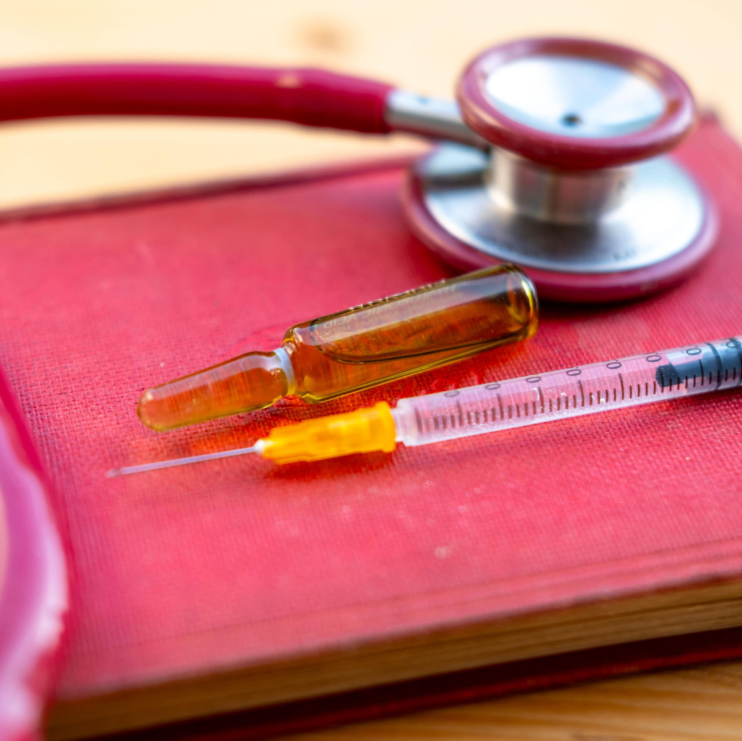 Une seringue, un stéthoscope et une fiole contenant du matériel d’injection sont posés sur un livre rouge représentant la loi.