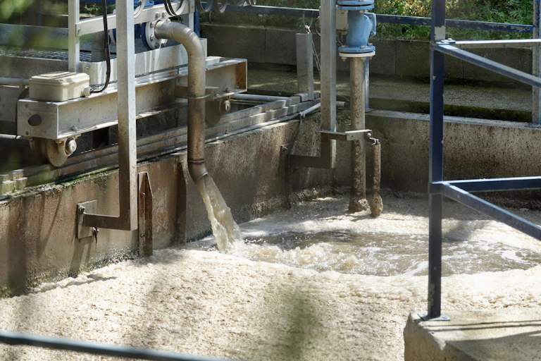 Agua de color marrón cae por una tubería a un tanque donde una espuma recubre la superficie del líquido