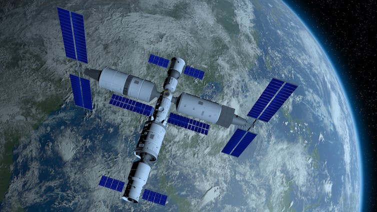A space station, which looks like several connected cylinders with solar panels coming off them, orbiting the planet Earth.