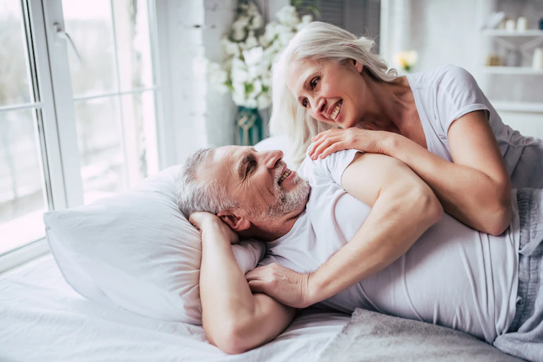 Una pareja de adultos mayores en la cama se miran y se sonríen.
