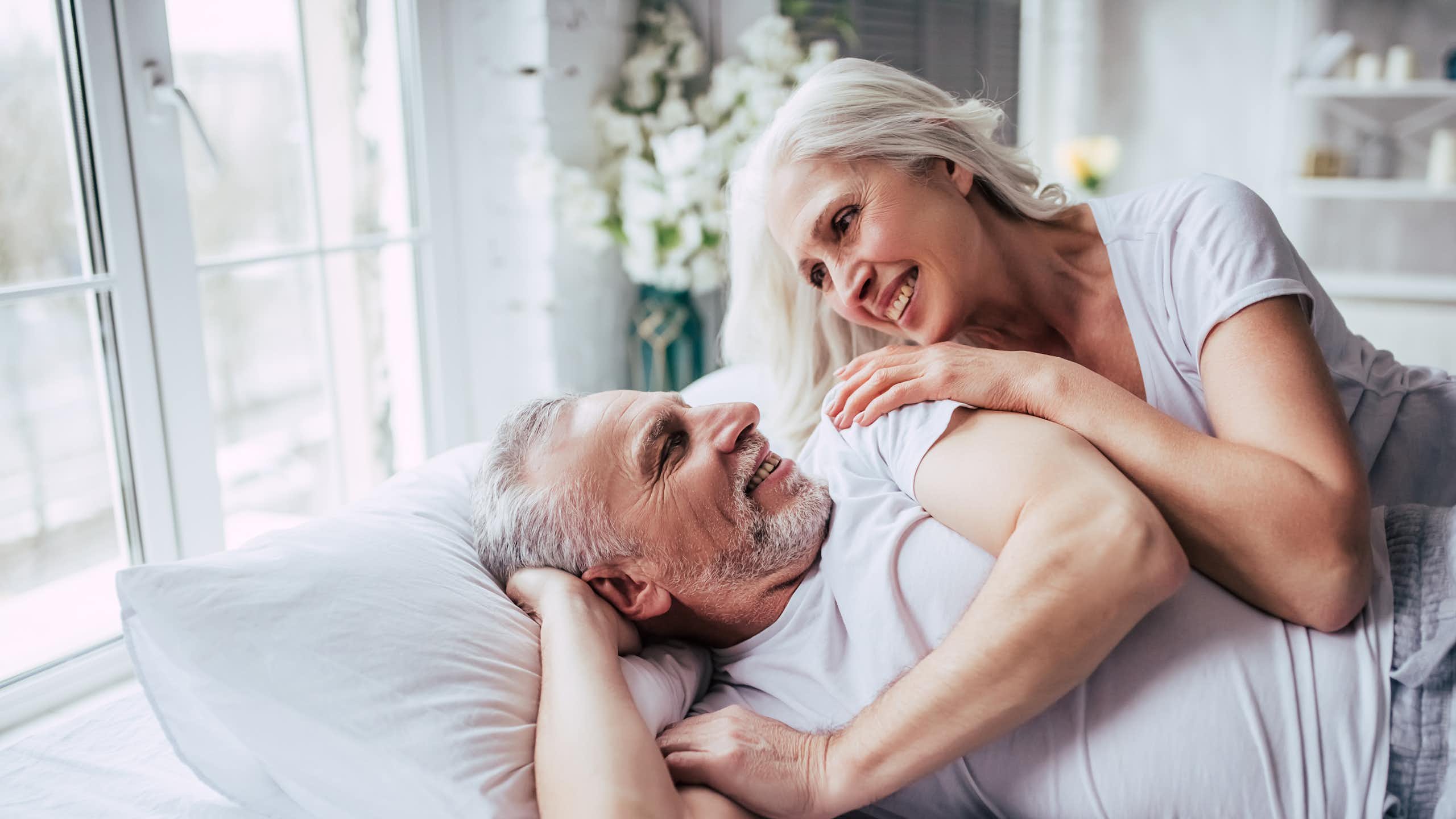 Una pareja de adultos mayores en la cama se miran y se sonríen.