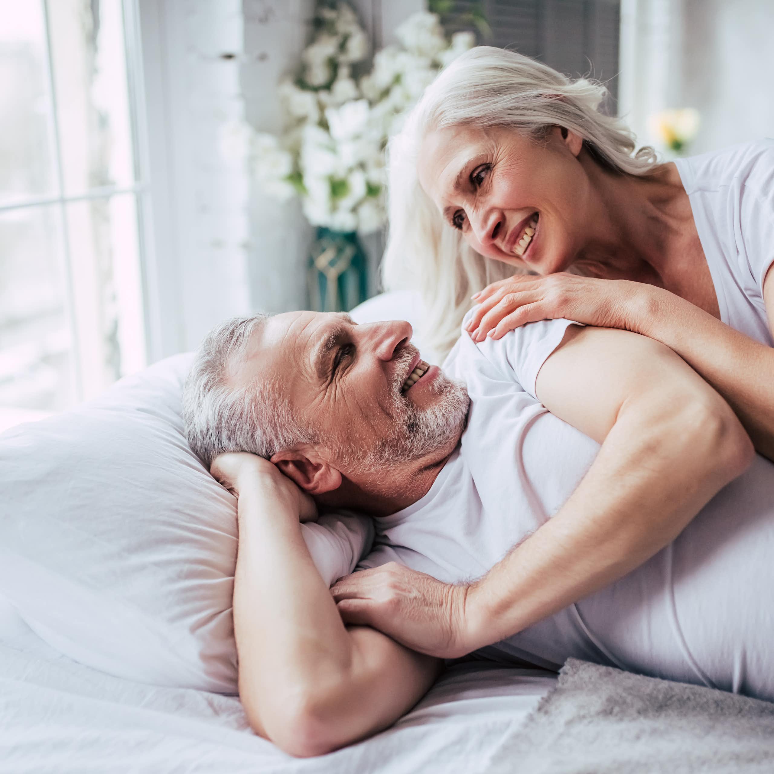 Una pareja de adultos mayores en la cama se miran y se sonríen.