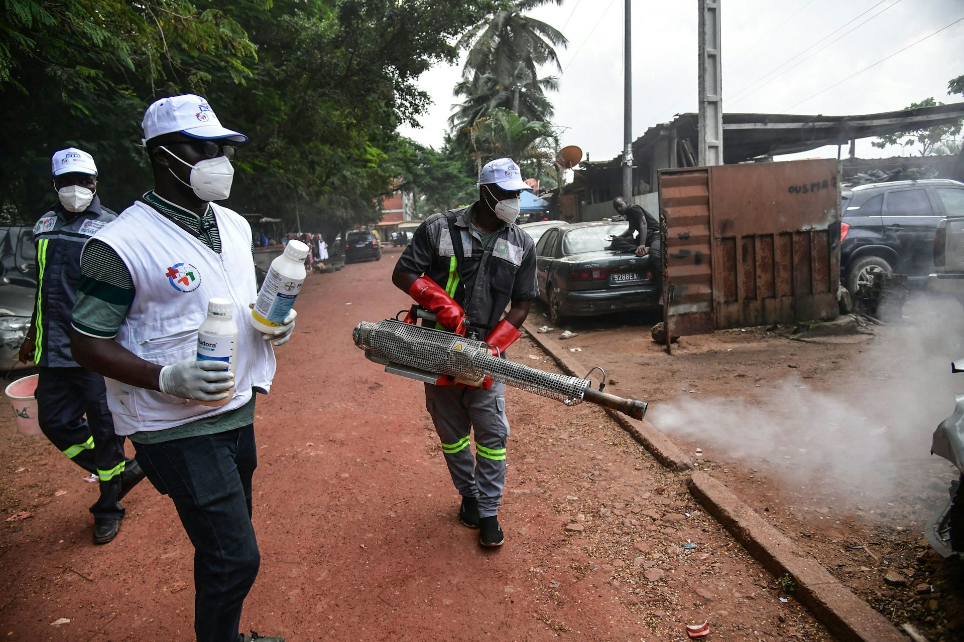 People in protective clothing and masks spray a smoky substance on the street