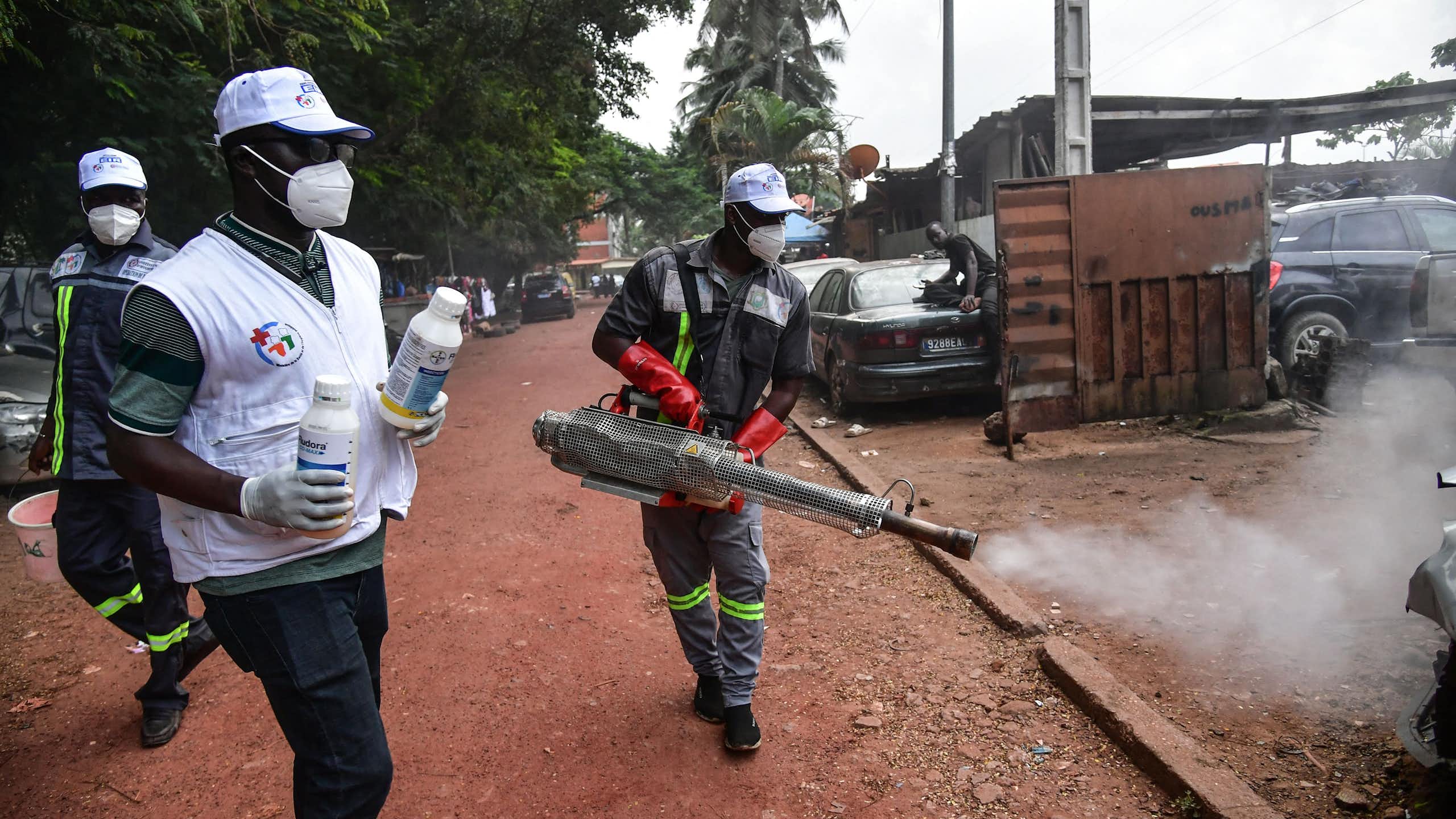 People in protective clothing and masks spray a smoky substance on the street