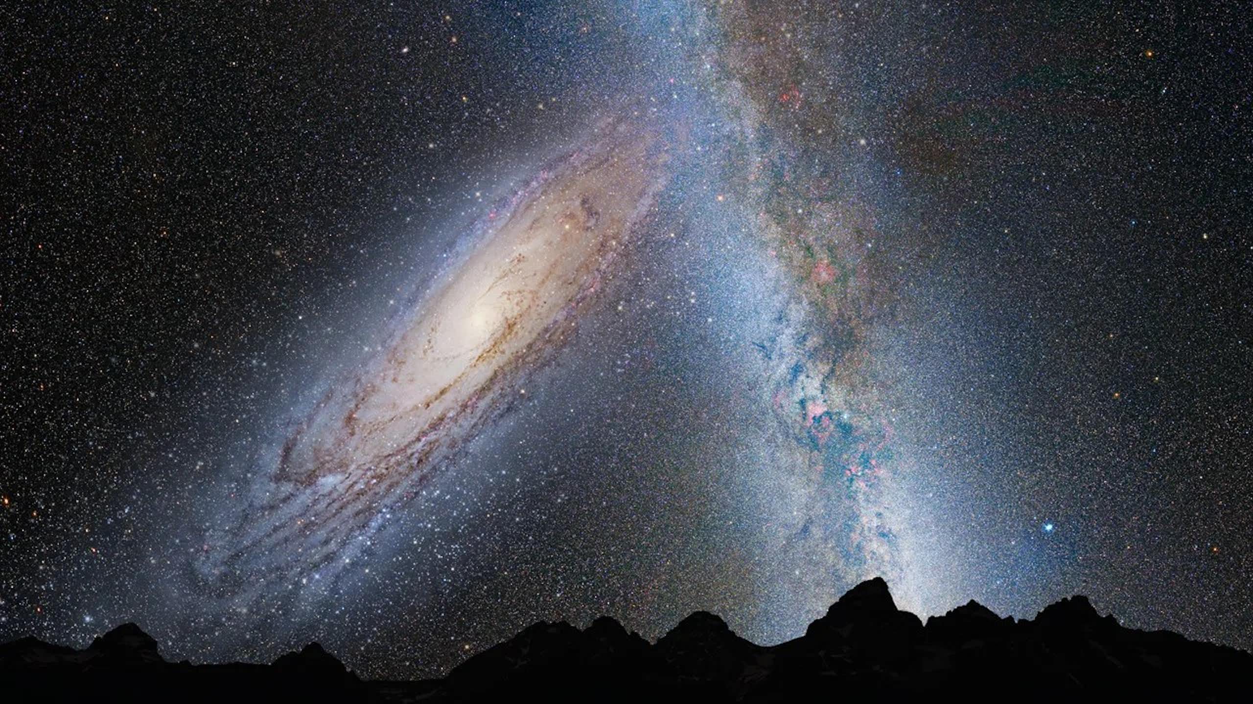 A spiral galaxy shown in the sky against the Milky Way, above a mountain range.