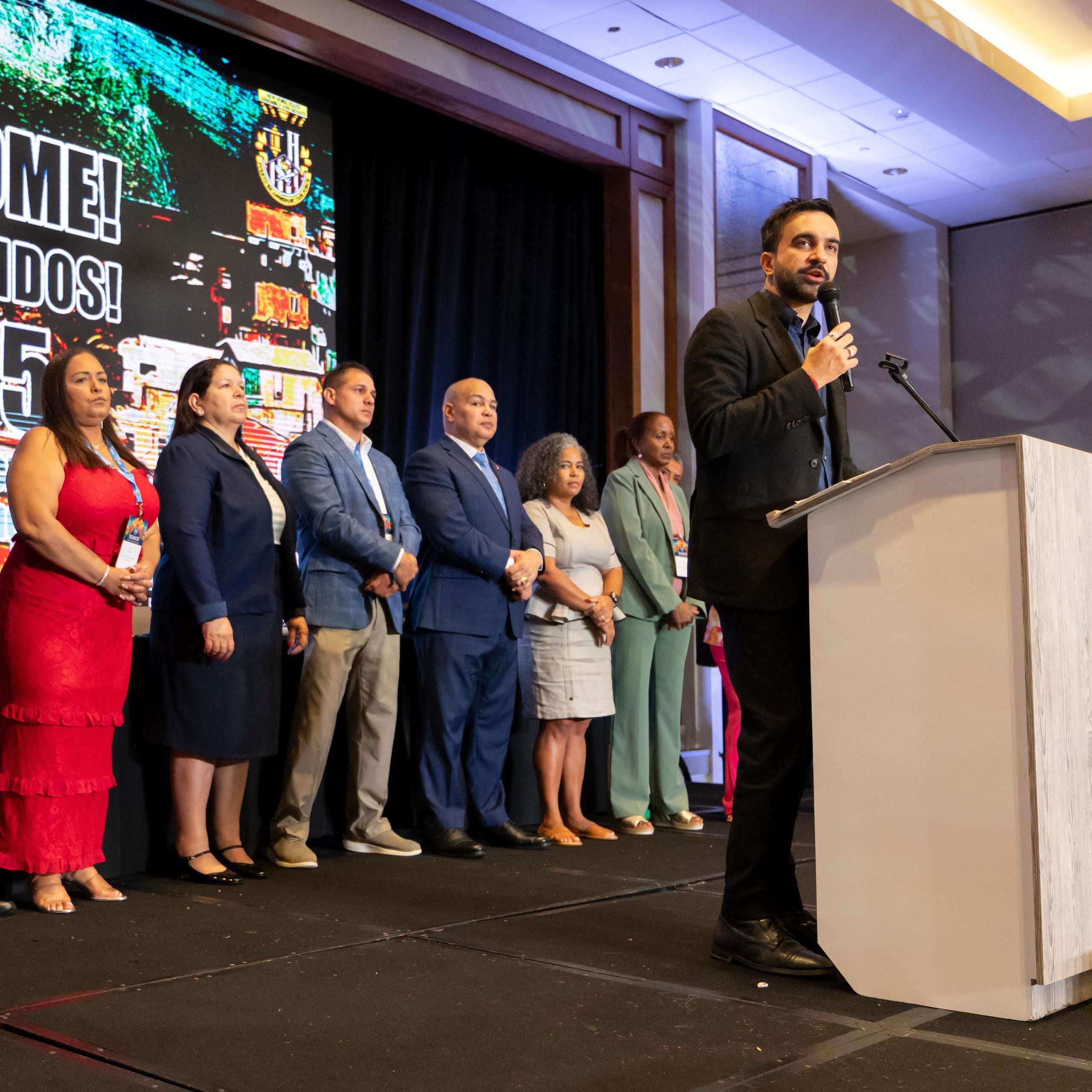 A man in front of a podium speaks to a crowd.