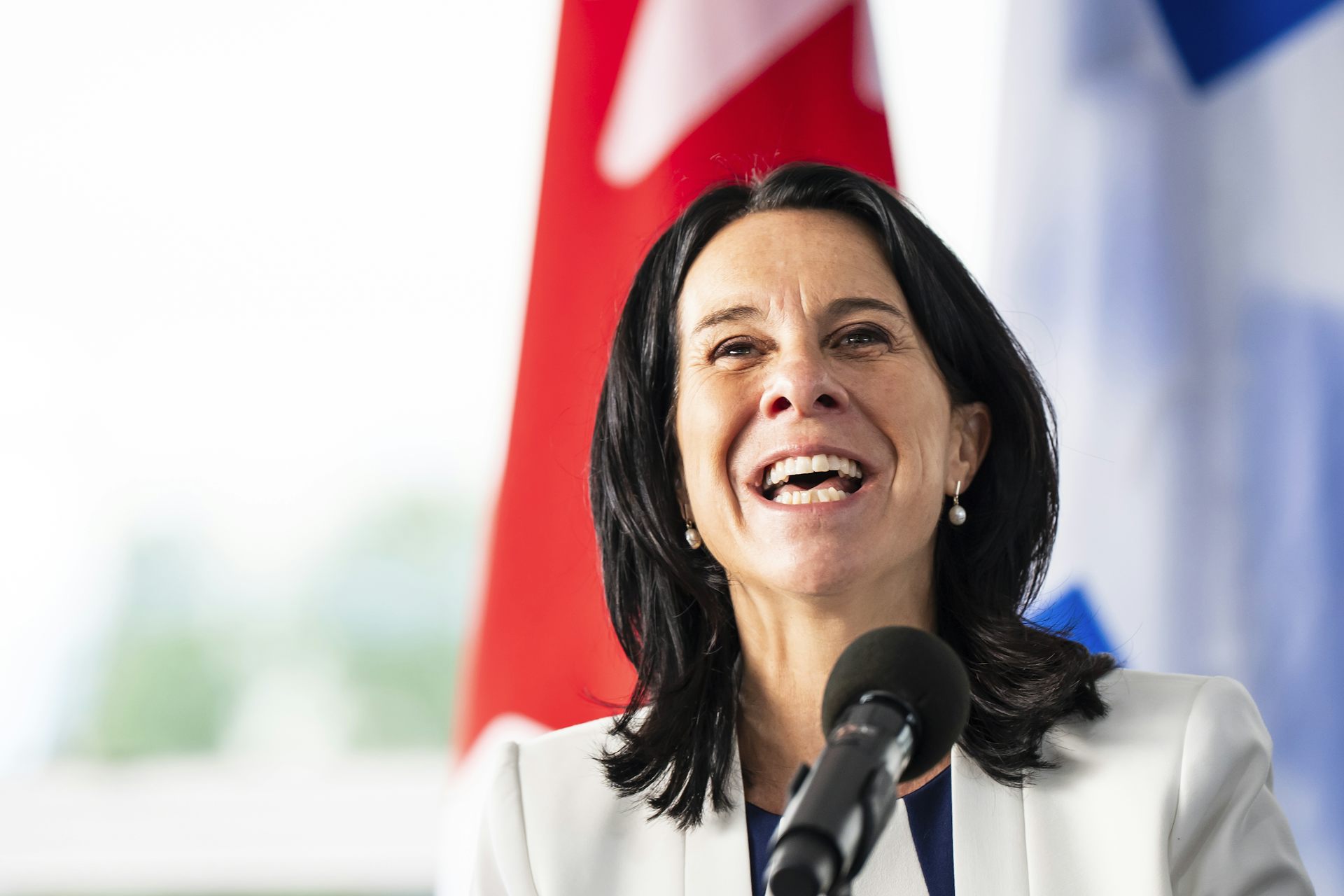 A dark-haired woman in a white jacket smiles broadly.