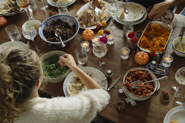 Personne prenant une cuillerée de petits pois sur une table chargée de plats de Thanksgiving