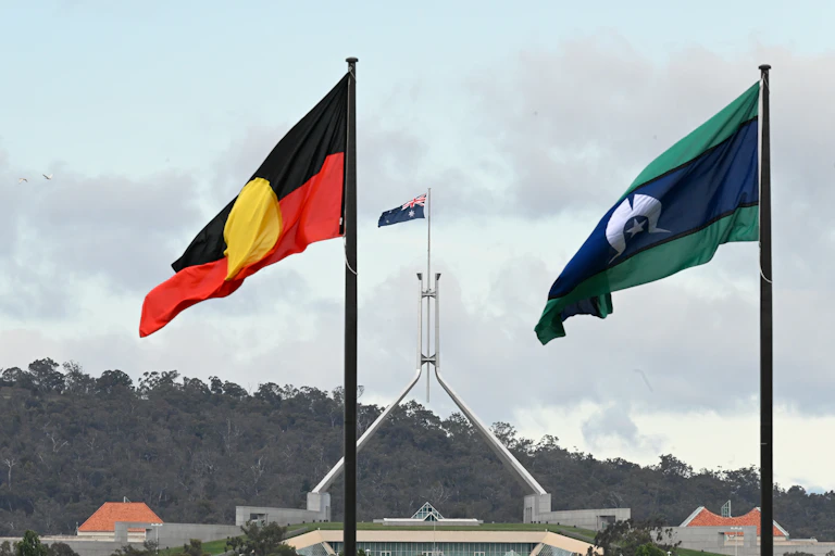 The Aboriginal and Torres Strait Islander flags flying in the foreground, with Parliament House, Canberra, in the background.