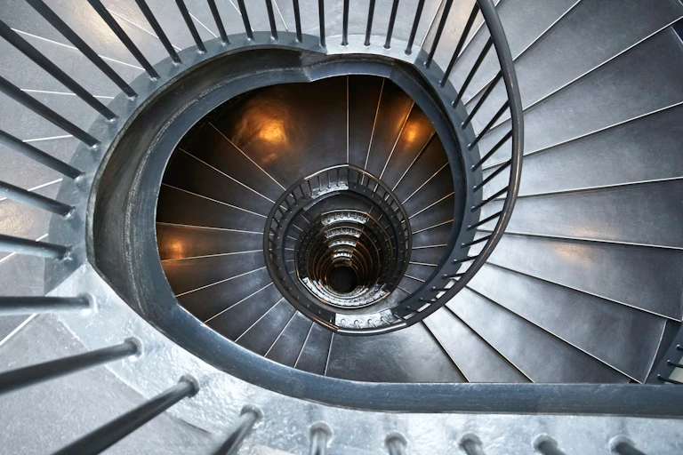 A steel spiral staircase leading down into a dark hole.