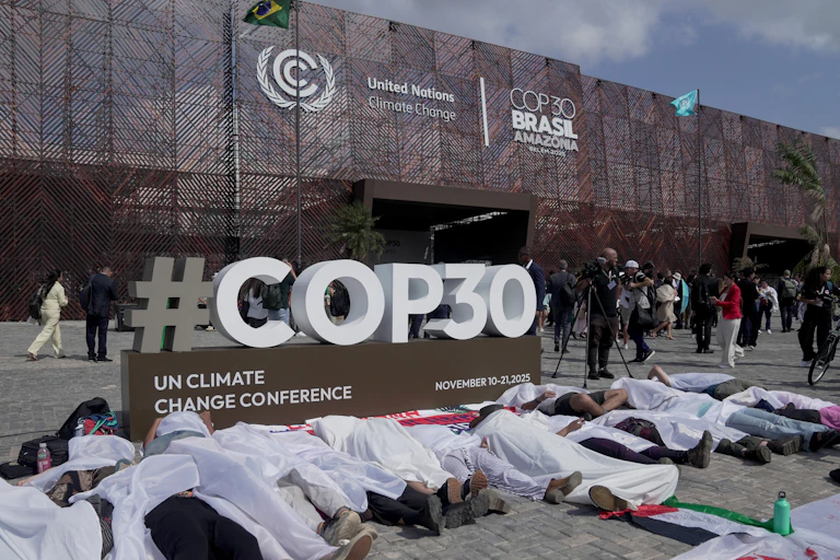 People lying down covered with white sheets in front of the COP30 sign as a form of protest