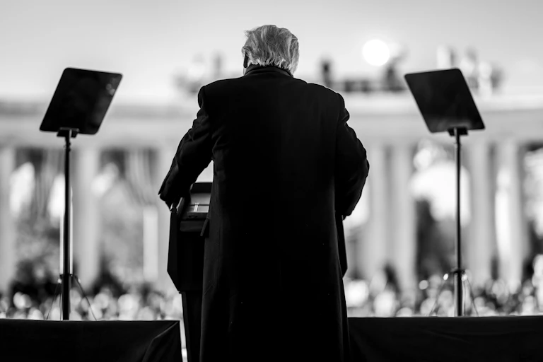 A black and white image of Donald Trump, taken from behind, speaking at the Memorial Amphitheater of Arlington National Cemetery to mark Veterans Day in the US.