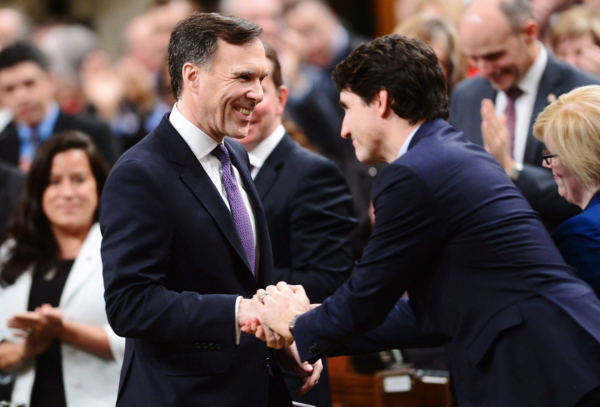 Two dark-haired men smile and shake hands in the House of Commons.