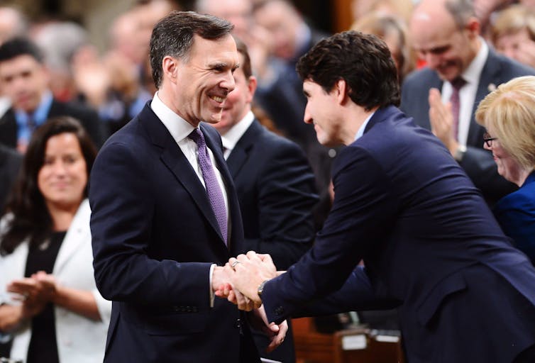 Two dark-haired men smile and shake hands in the House of Commons.