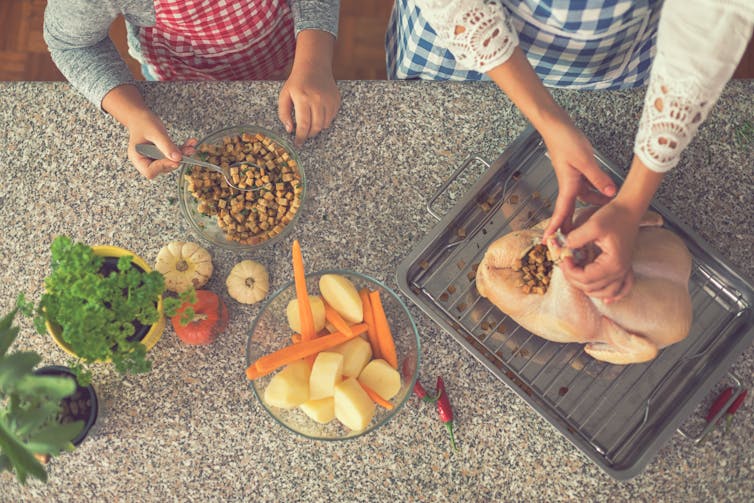 A turkey on a counter being stuffed by two sets of hands.