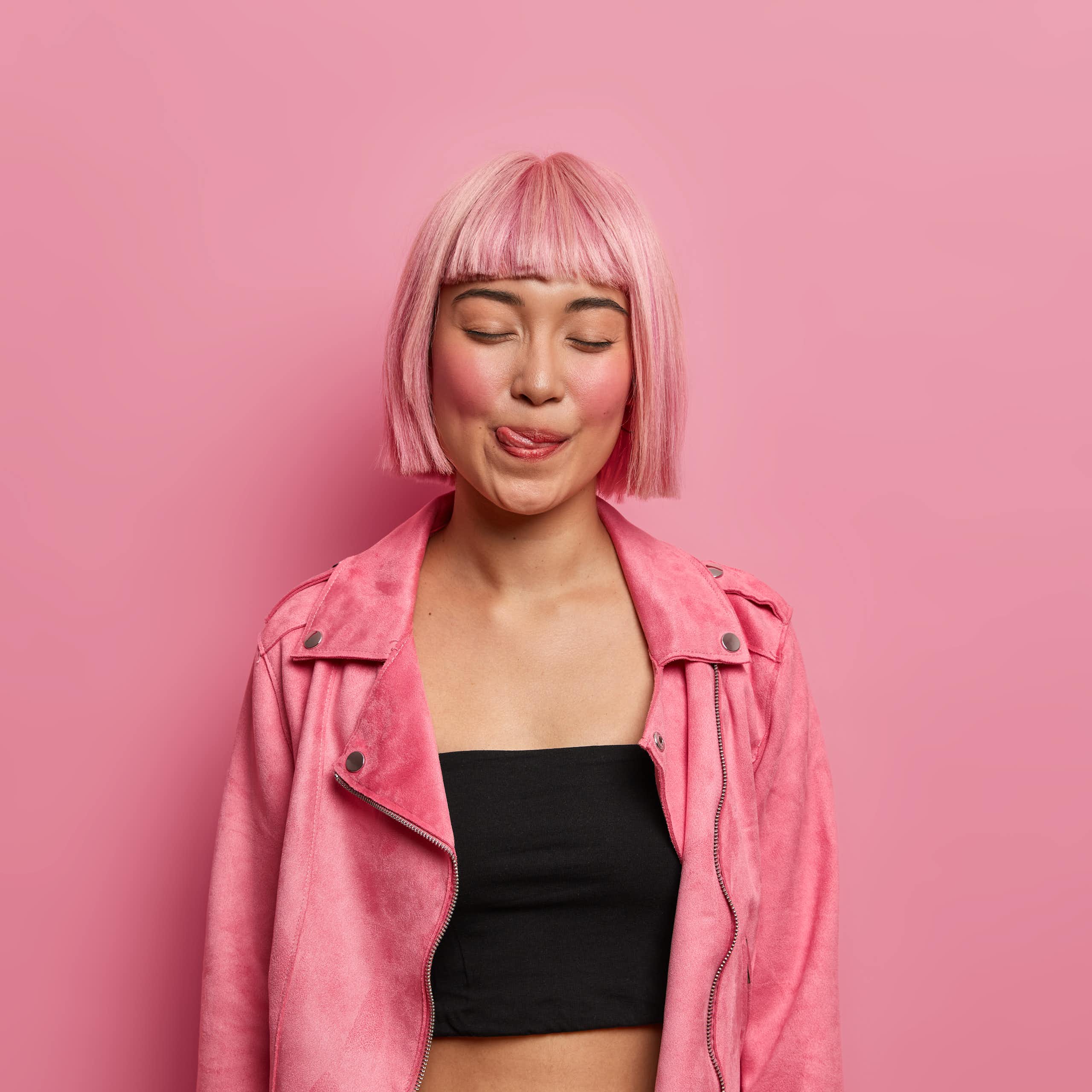 Girl with pink hair against pink background licking her lips.