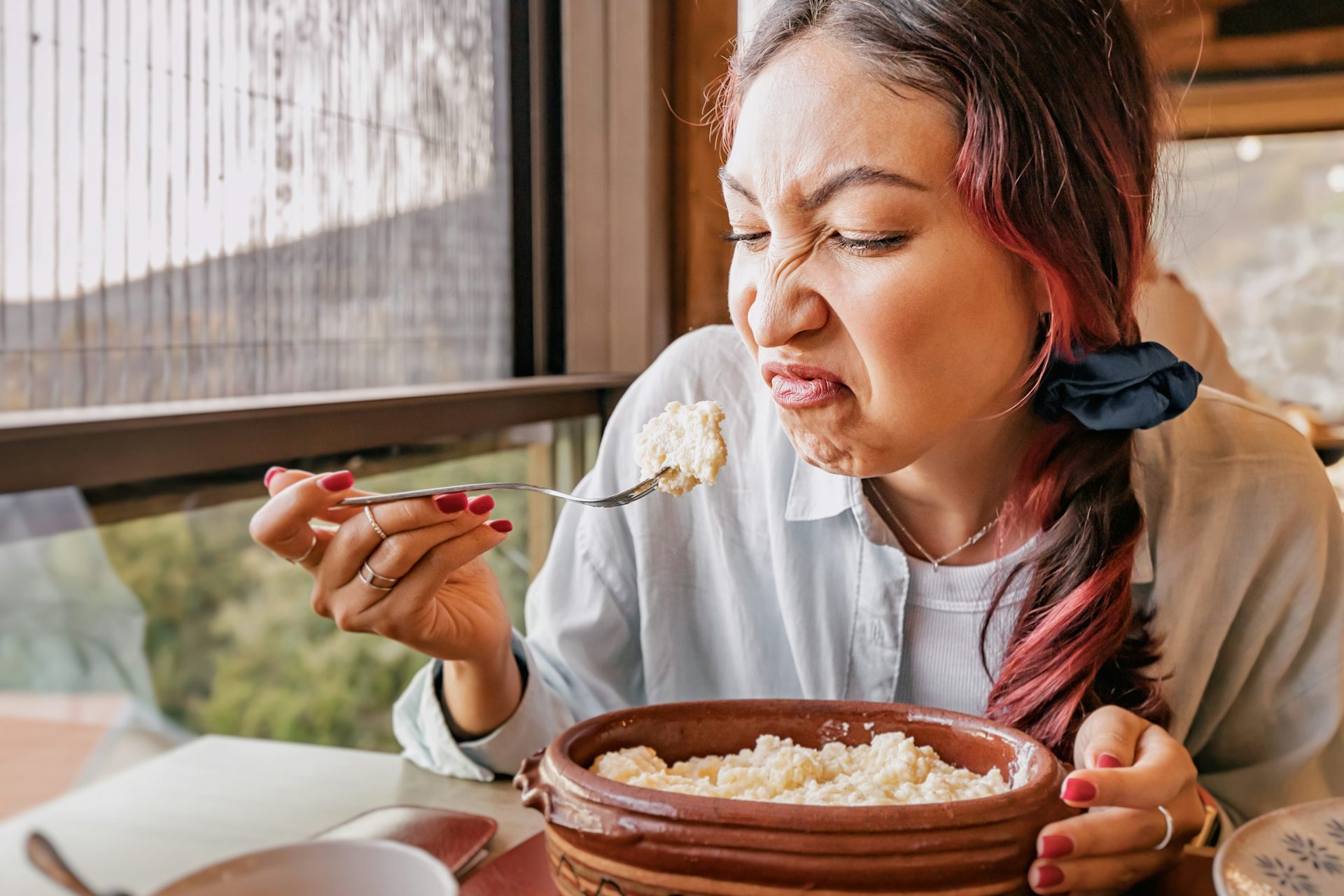 Woman sitting eating at a restaurant with a disgusted expression on her face.