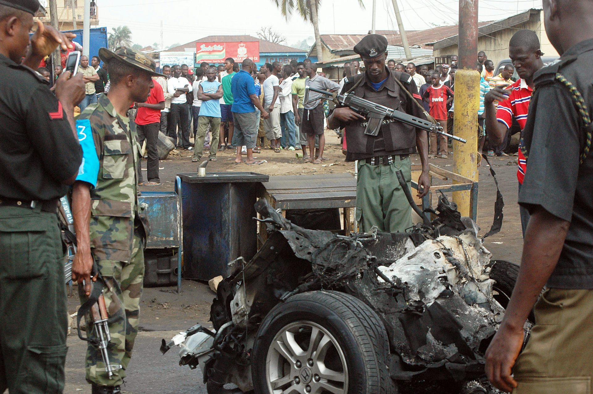 Men in police and army uniform looking at a burnt car 