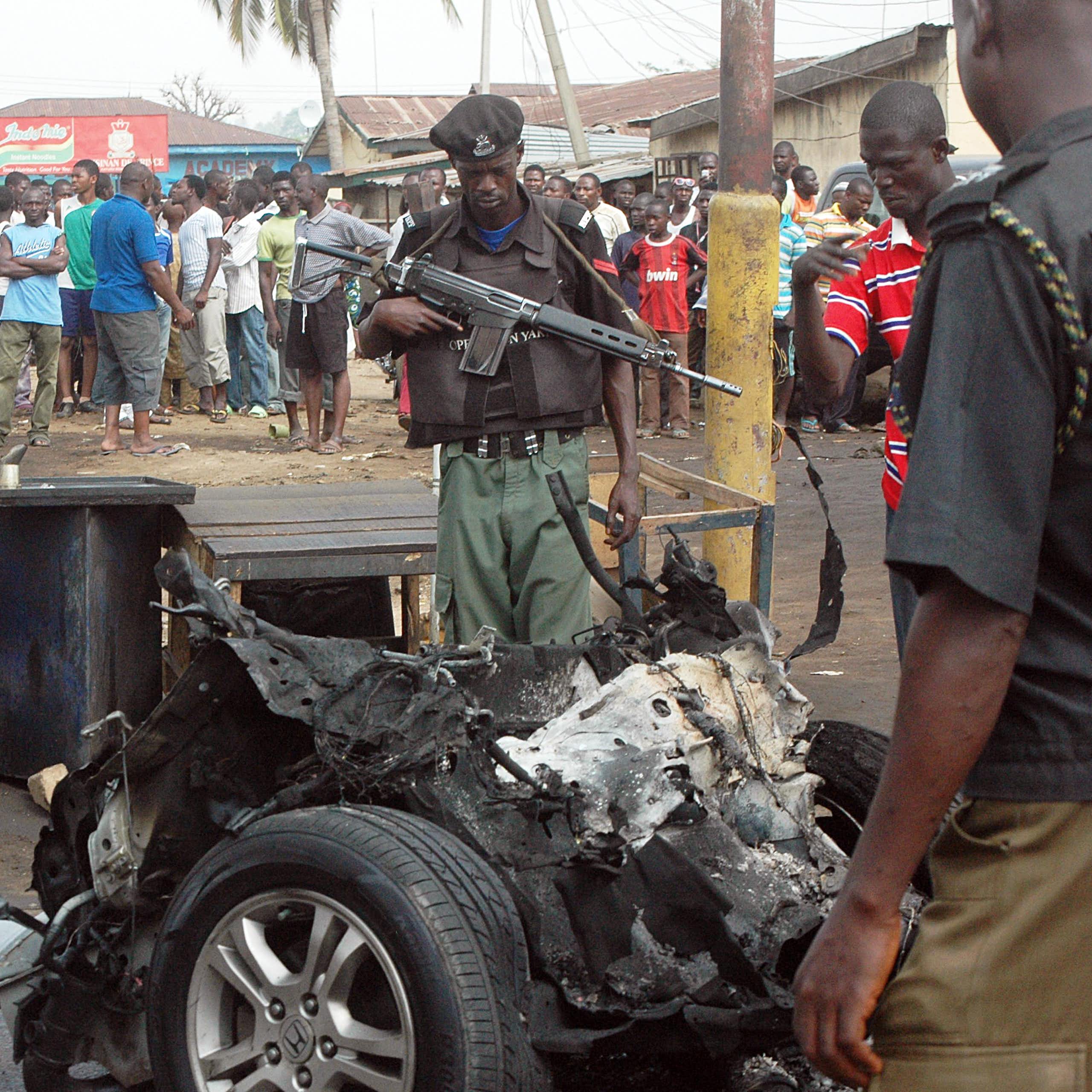 Men in police and army uniform looking at a burnt car