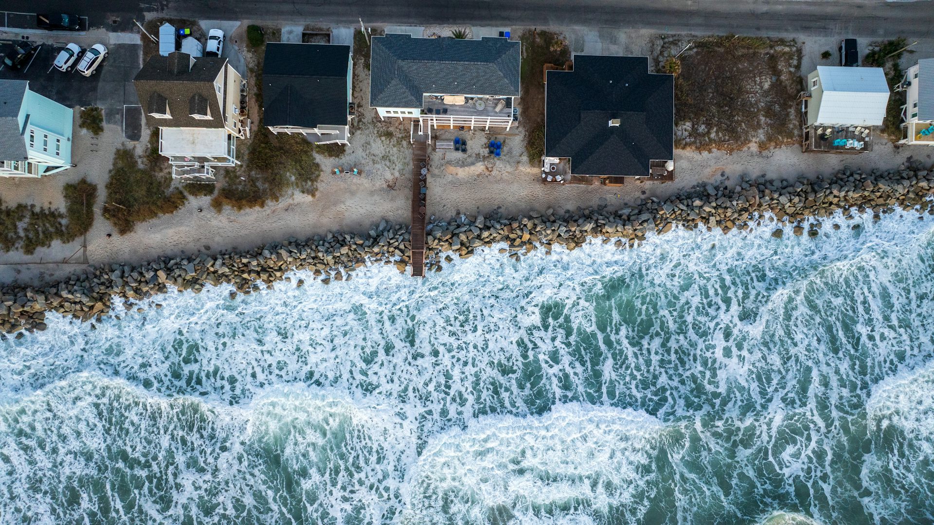 aerial shot of sea and coastal properties with waves hitting sea wall