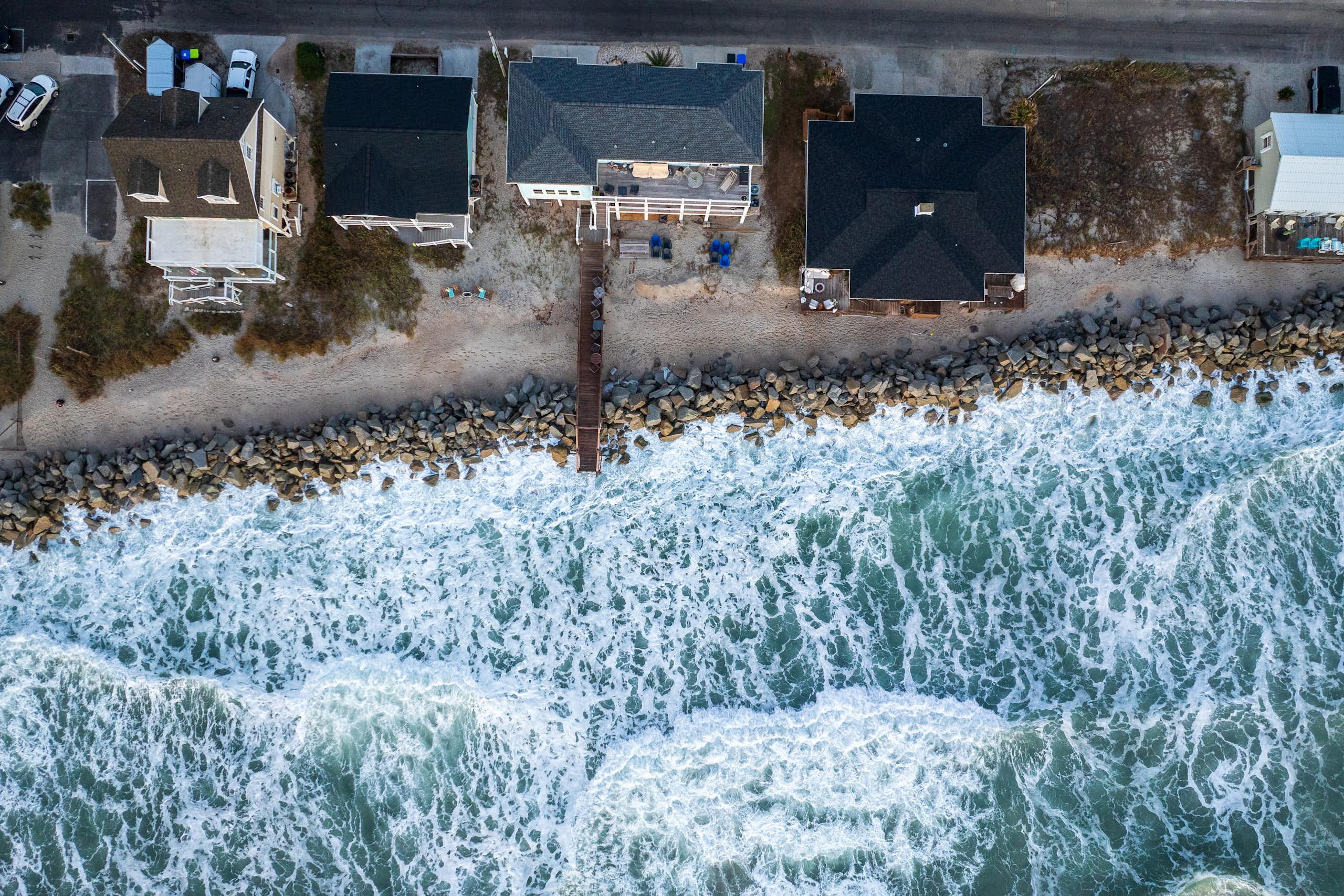 aerial shot of sea and coastal properties with waves hitting sea wall