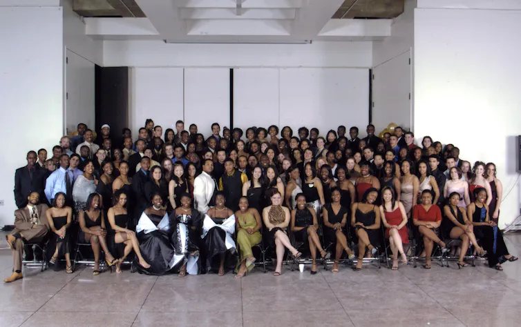 A large group of young people dressed in formal clothing all pose together and smile.