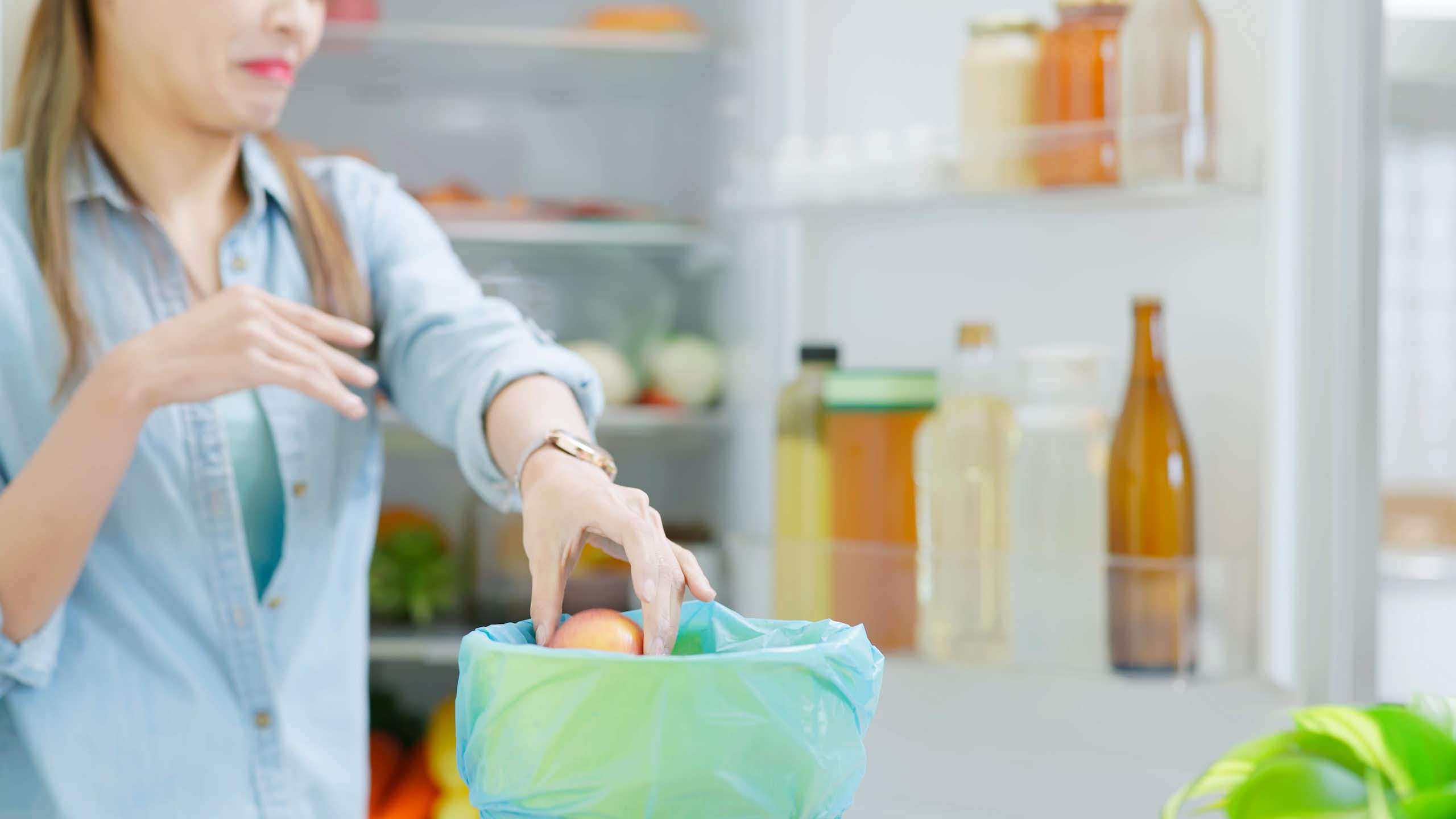 Une femme nettoie son réfrigérateur et jette dans un seau des aliments qui sentent mauvais.